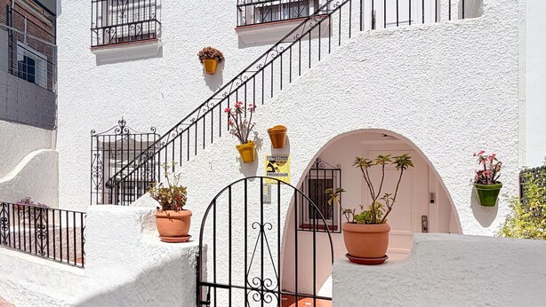 A white building with a staircase, potted plants, and a gated entrance. - Escuela Village | Budget Quadruple Apartment (Marbella)