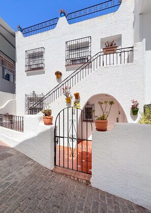 Un edificio blanco con escaleras, plantas en macetas y una entrada protegida por una reja.