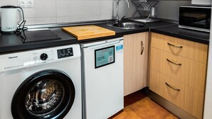 A compact kitchen with wooden cabinets, a washing machine, a microwave, and a sink. - Escuela Village | Budget Quadruple Apartment (Marbella)