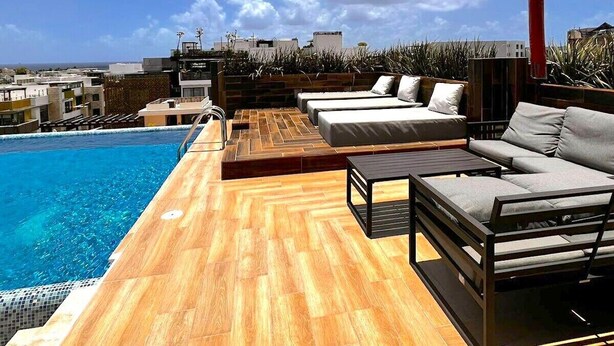 Un área de piscina en la azotea con suelo de madera, una piscina y un espacio de descanso con sofás y una mesa.