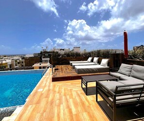 Un área de piscina en la azotea con suelo de madera, una piscina y un espacio de descanso con sofás y una mesa.