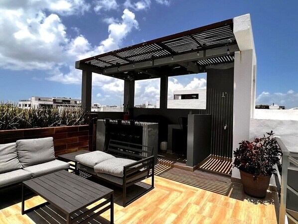 Un espacio al aire libre con piso de madera, un sofá, una mesa y una estación de parrilla.