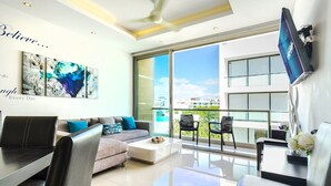 Un salón moderno con sofá, mesa de centro y sillas. Se ve una ventana grande con vistas a edificios y zonas verdes.