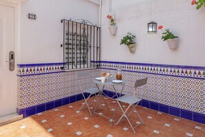 Un pequeño patio con una mesa, sillas, un portón de metal y plantas en macetas.