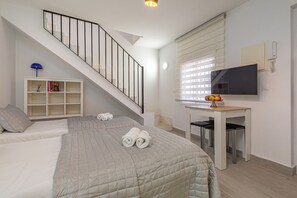 A bedroom with a bed, a desk, a television, a bookshelf, and a staircase.