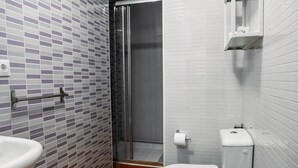 Un baño con suelo de baldosas, inodoro, lavabo y zona de ducha.