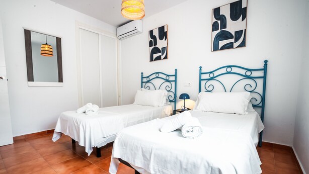 Habitación de hotel con dos camas, ropa de cama blanca, una lámpara colgante y arte abstracto en la pared.