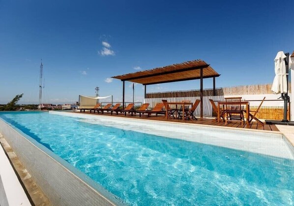 Piscina con sillas de descanso y un área de estar techada.