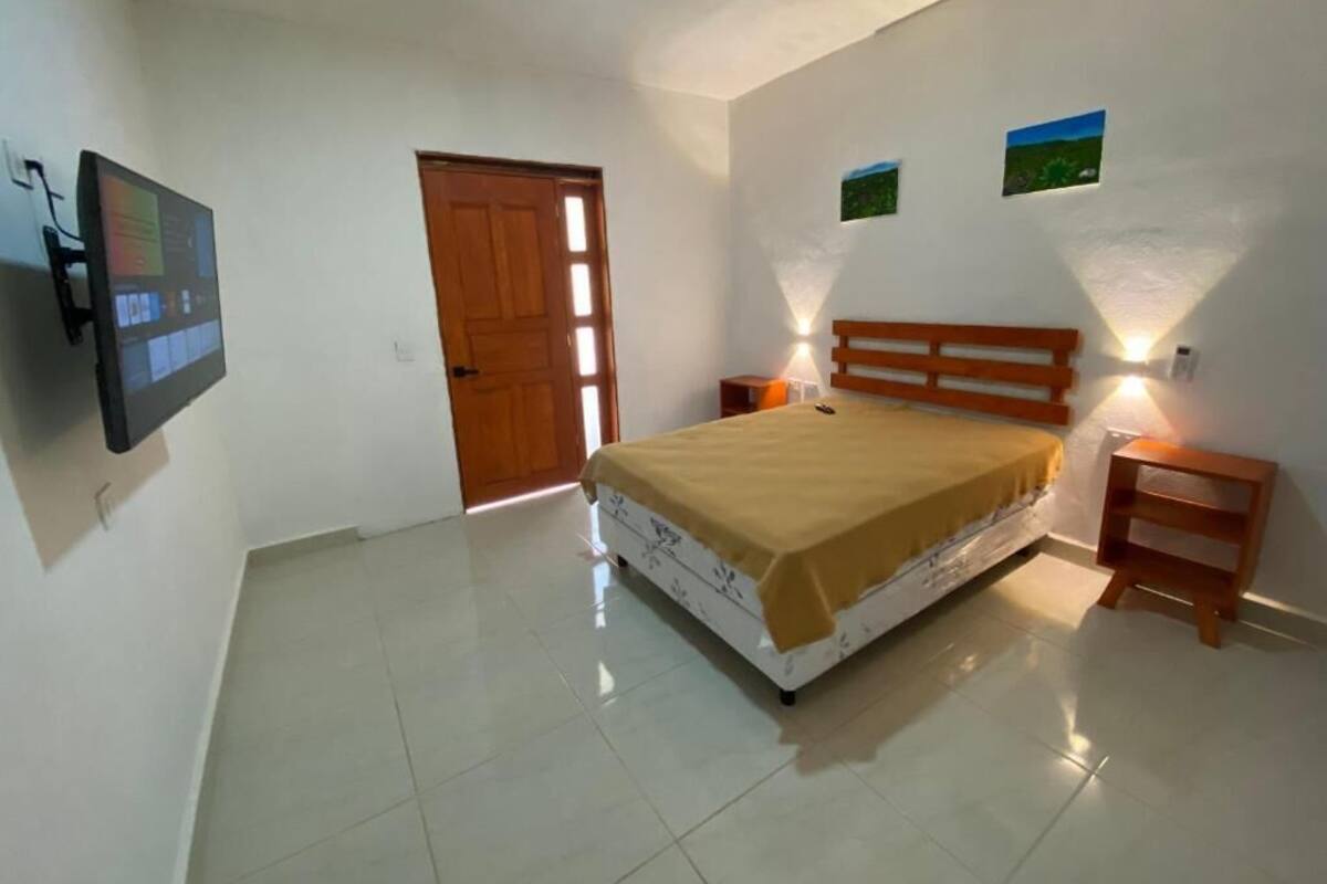 A bedroom with a bed, a television mounted on the wall, a door, and two wall-mounted lamps.