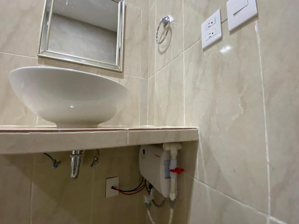 Un baño con lavamanos blanco, espejo y perchero.