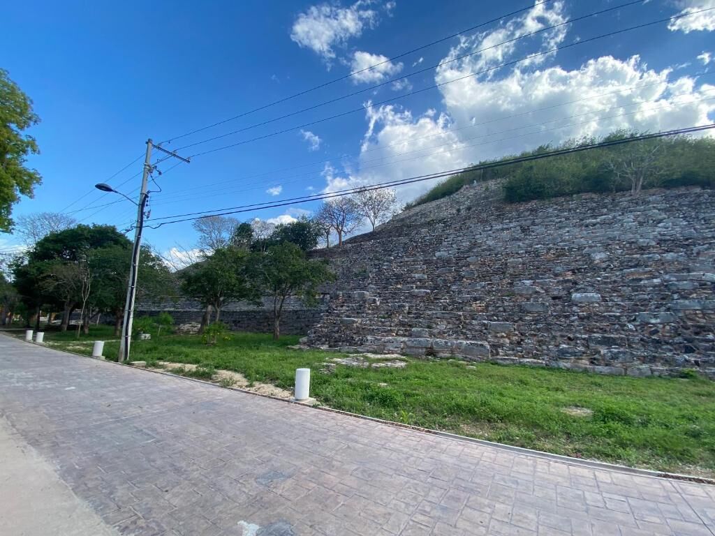 Un sendero pavimentado que conduce a un muro de piedra, con césped y árboles.