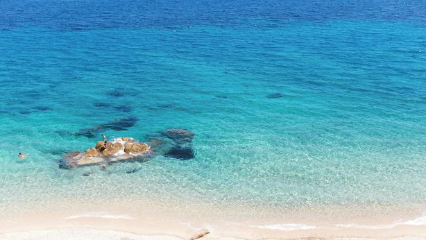 Una playa con agua turquesa cristalina, zona rocosa y orilla arenosa.