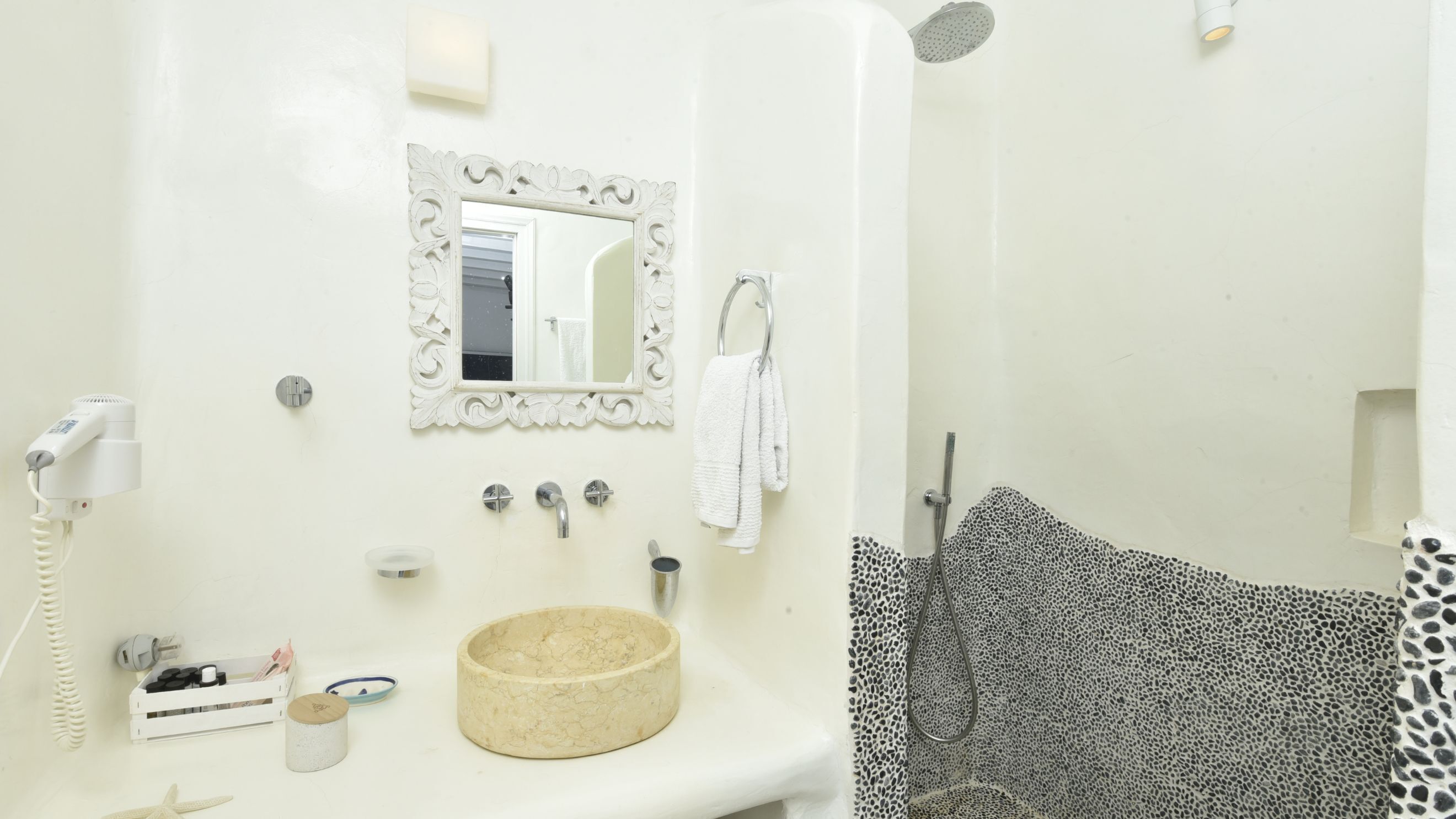 A bathroom with a round sink, a mirror with an ornate frame, a towel rack, a shower with a leopard print shower curtain, and a hairdryer on the wall.
