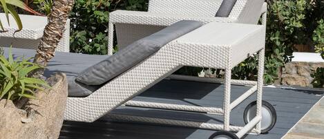 Una silla de mimbre blanca con cojín gris, ubicada en una terraza con borde de piedra.