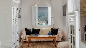 Una habitación acogedora con una mesa de madera, un sofá con cojines, un armario blanco y una ventana con vistas al paisaje.