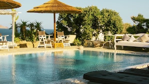 Zona de piscina con sillones de descanso, sombrillas y vista al océano.