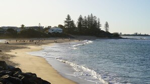 A beach with people, a sandy shore, and a building in the background. - Moffat Beach Coastal Contemporary Unit B (Moffat Beach)