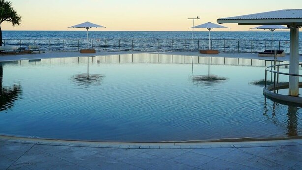 A pool with a view of the sea, surrounded by umbrellas and lounge chairs. - Moffat Beach Coastal Contemporary Unit B (Moffat Beach)