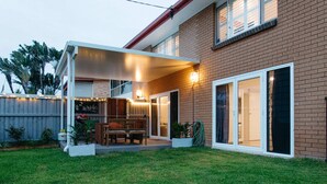 A residential building with a covered patio, a brick exterior, and a sliding glass door. - Moffat Beach Coastal Contemporary Unit B (Moffat Beach)