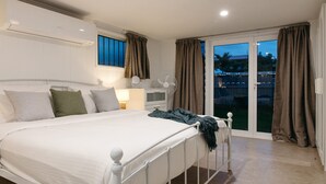 A bedroom with a bed, bedside table, lamp, air conditioning unit, and a view through a sliding glass door. - Moffat Beach Coastal Contemporary Unit B (Moffat Beach)