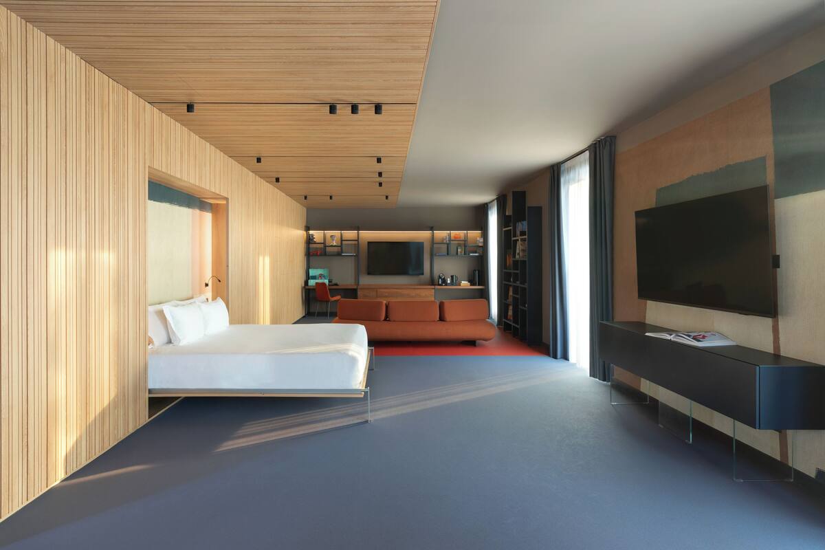 A modern hotel room with a bed, a sofa, a TV, and a desk.