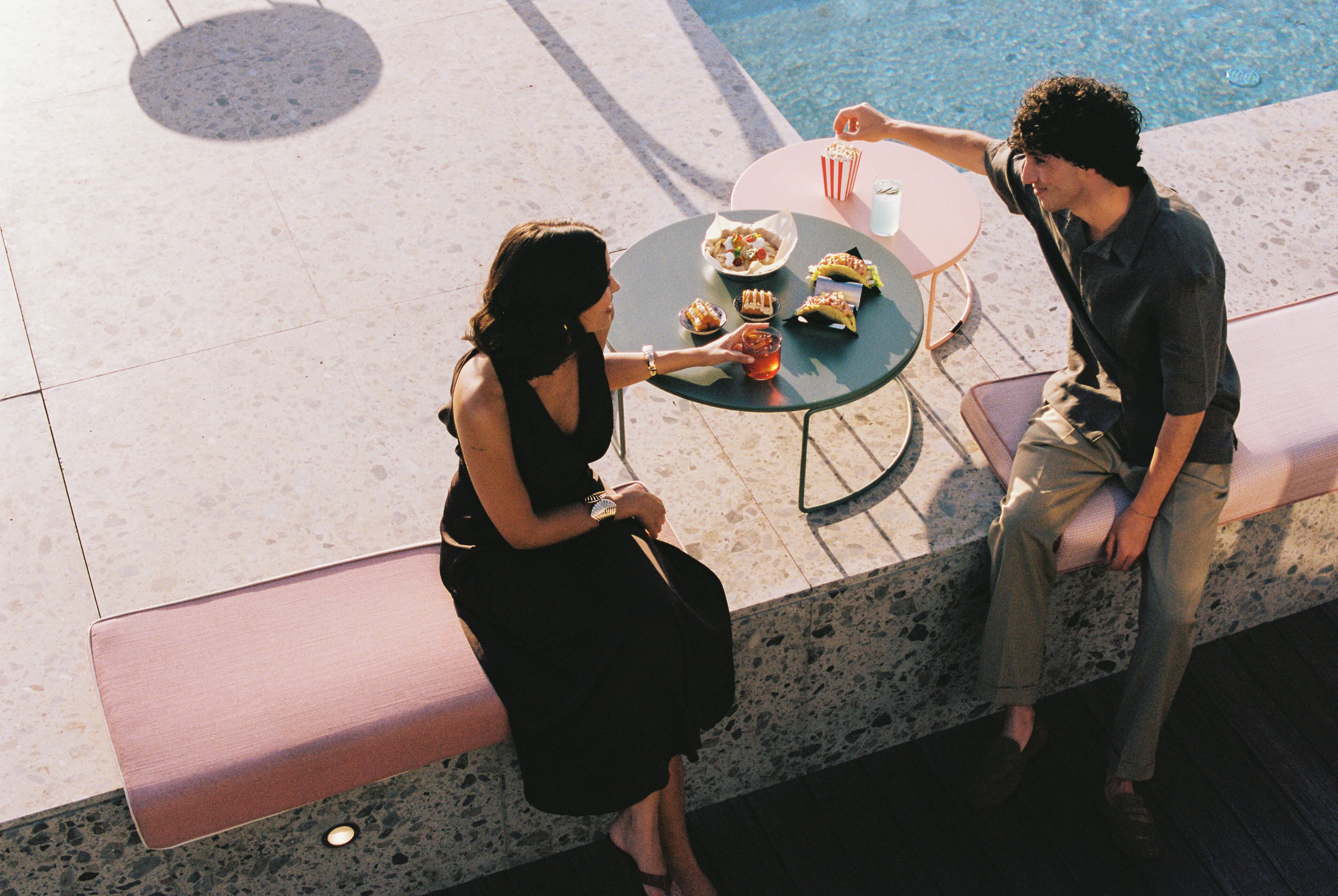 Two people seated at an outdoor table with a pool in the background.