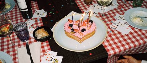 A table with a checkered tablecloth, a cake with candles, playing cards, and glasses of wine.