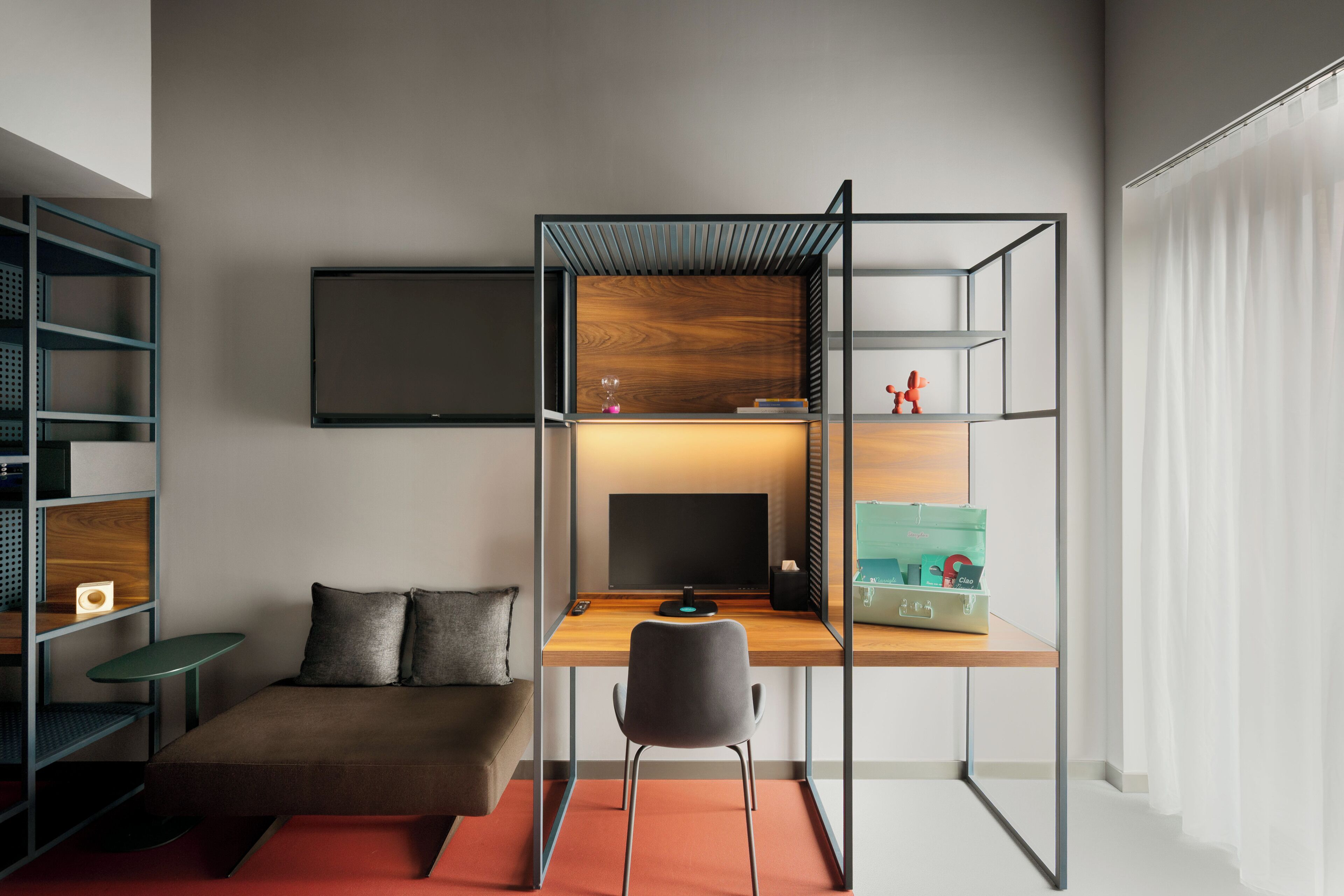 A modern room with a desk, chair, sofa, and shelves.