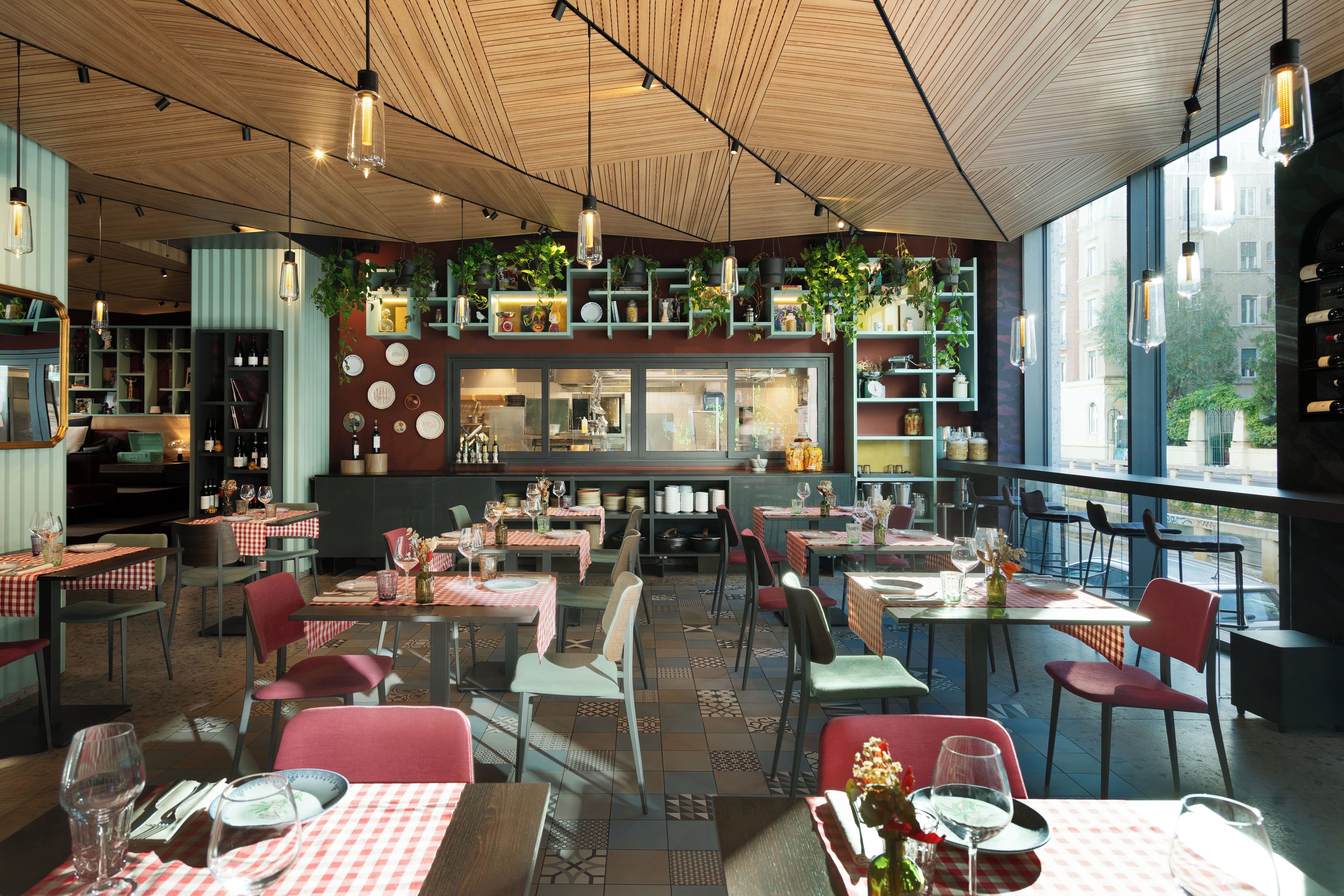 Interior de restaurante con varias mesas, sillas y plantas colgantes.