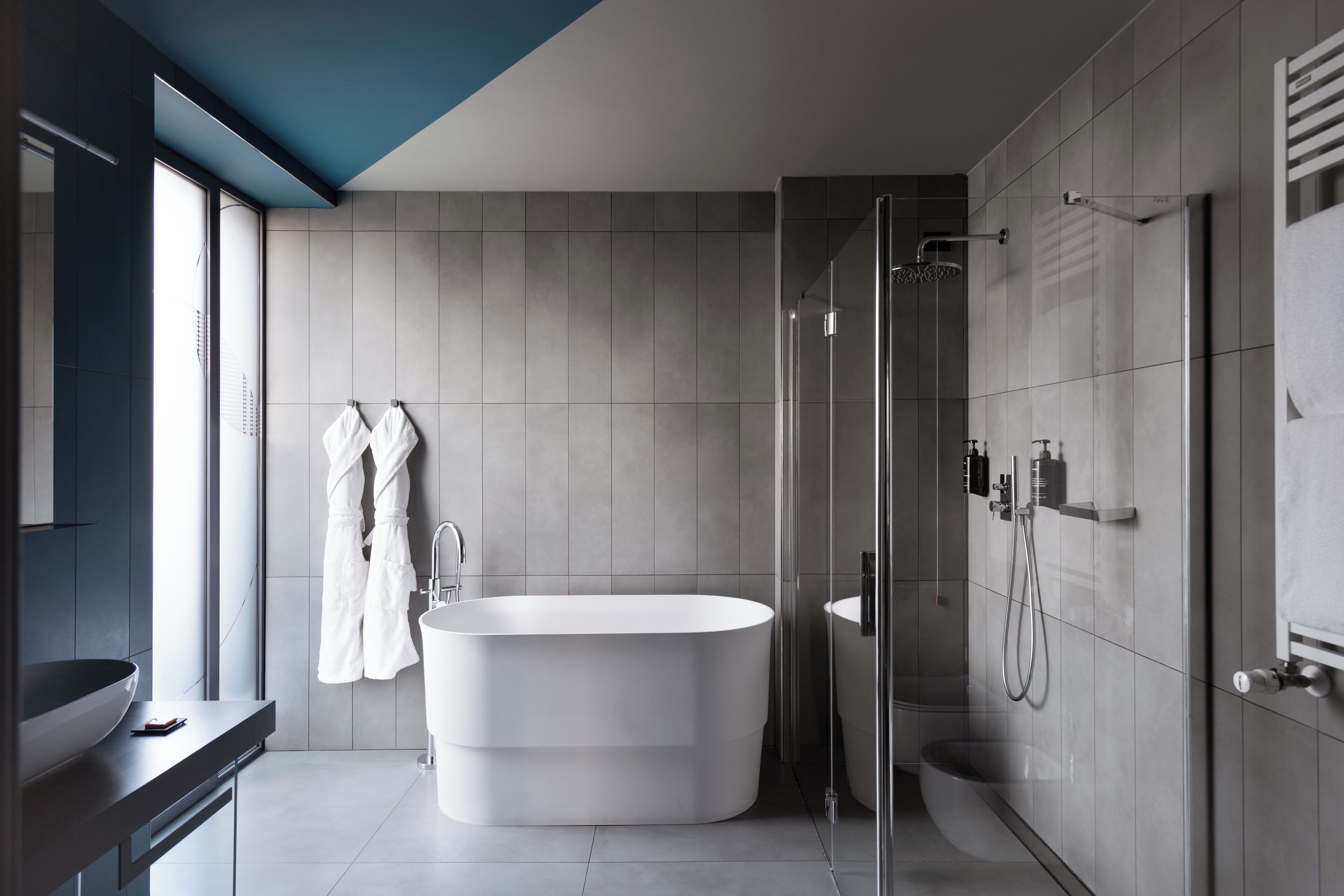 Un baño moderno con una bañera independiente, ducha con mampara de vidrio y un amplio ventanal que proporciona luz natural.