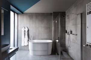 A modern bathroom with a freestanding bathtub, a glass-enclosed shower, and a large window providing natural light.