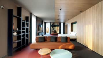 Une chambre d’hôtel moderne avec un canapé, deux petites tables rondes, une bibliothèque et un lit.