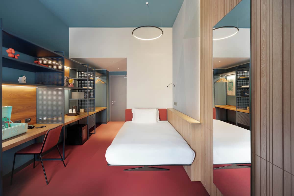 A modern hotel room with a bed, desk, and wardrobe.