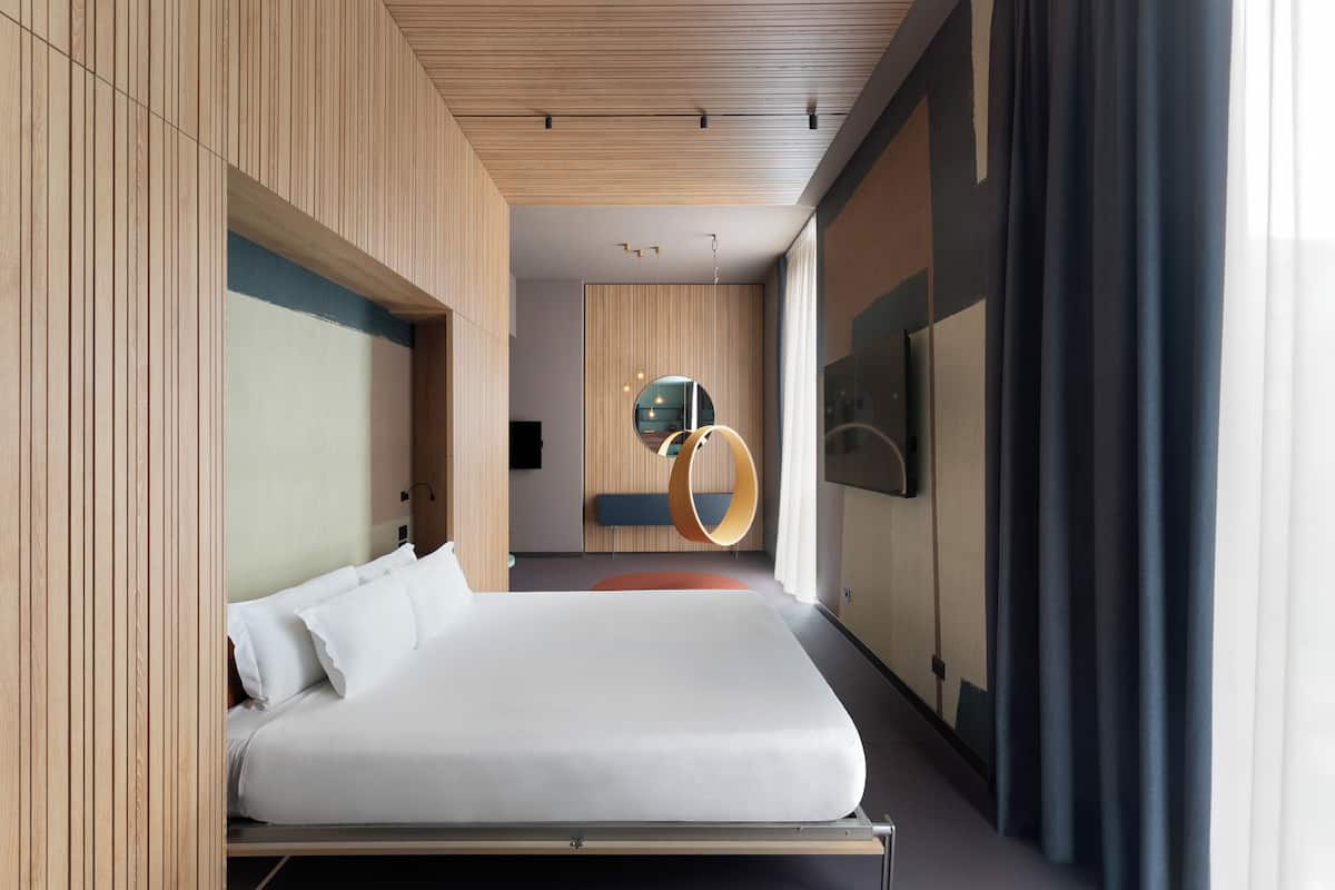 A modern hotel room with a large bed, wooden paneling, a circular light fixture, and a television.