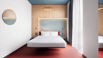 A modern hotel room with a bed, a round mirror, a headboard with built-in lighting, and a red carpet.