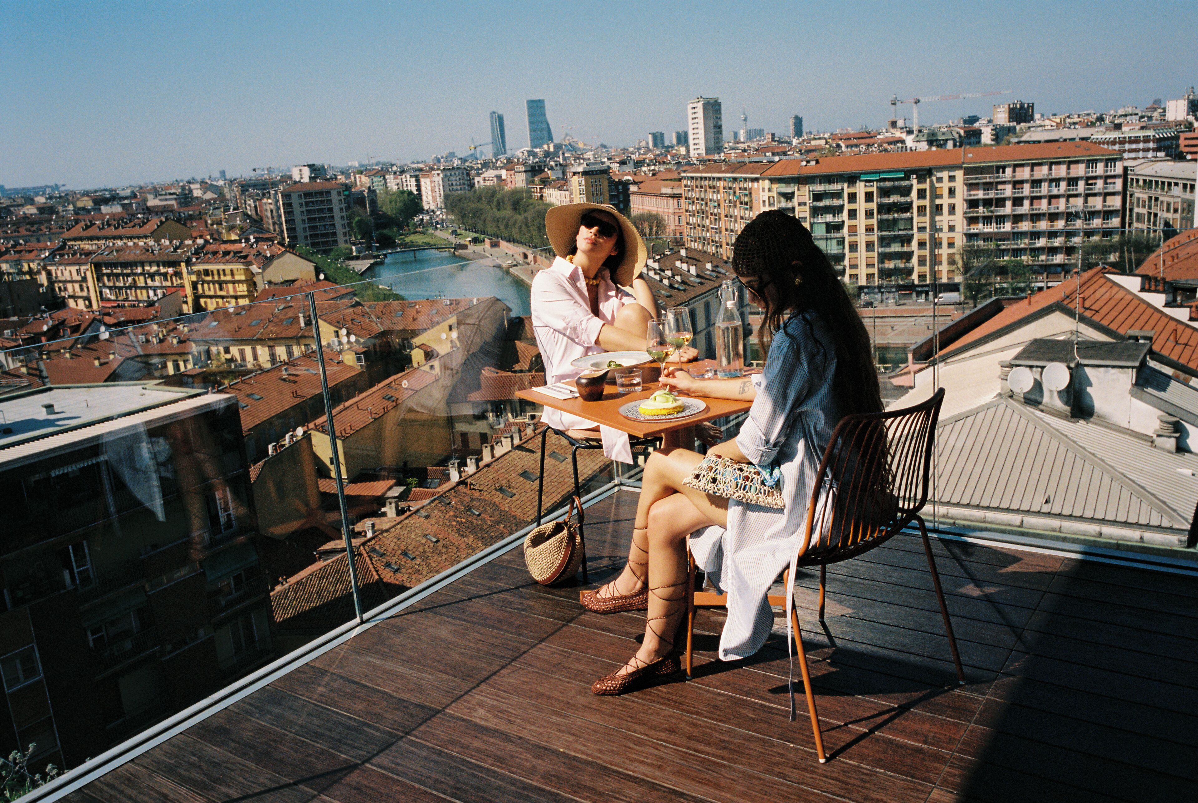 Un balcón en un edificio alto con una mesa, sillas y vistas a un paisaje urbano.