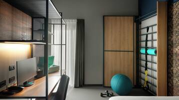Habitación de hotel moderna con escritorio, computadora, pelota de ejercicios y un perchero en la pared con toallas.