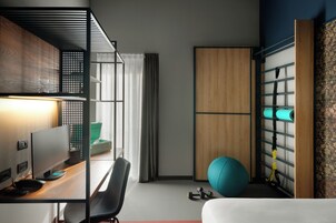 Een moderne hotelkamer met een bureau, computer, fitnessbal en een wandrek met handdoeken.