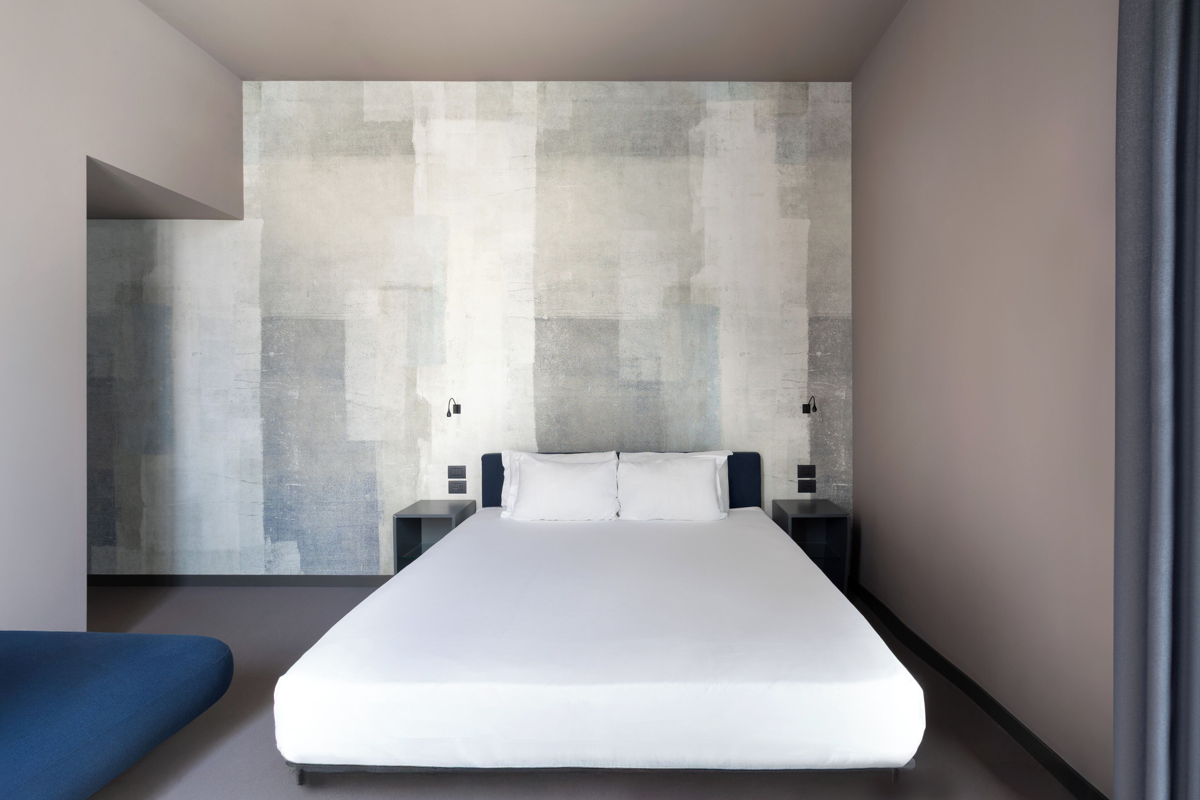 A modern hotel room with a large bed, bedside tables, and a large abstract wall art piece.