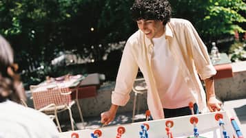 Iemand speelt tafelvoetbal buiten, met een tafel en stoelen op de achtergrond.