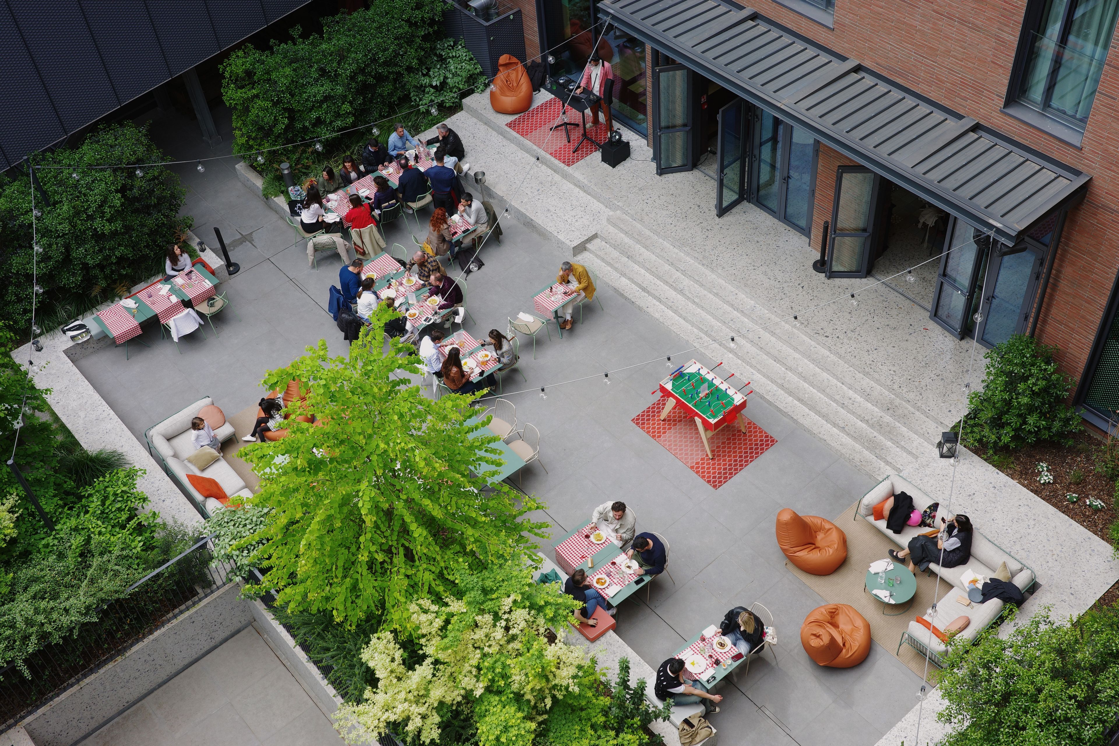 Un espace extérieur aménagé avec des tables et des chaises, un baby-foot, ainsi qu’un mélange de verdure et d’éléments architecturaux.