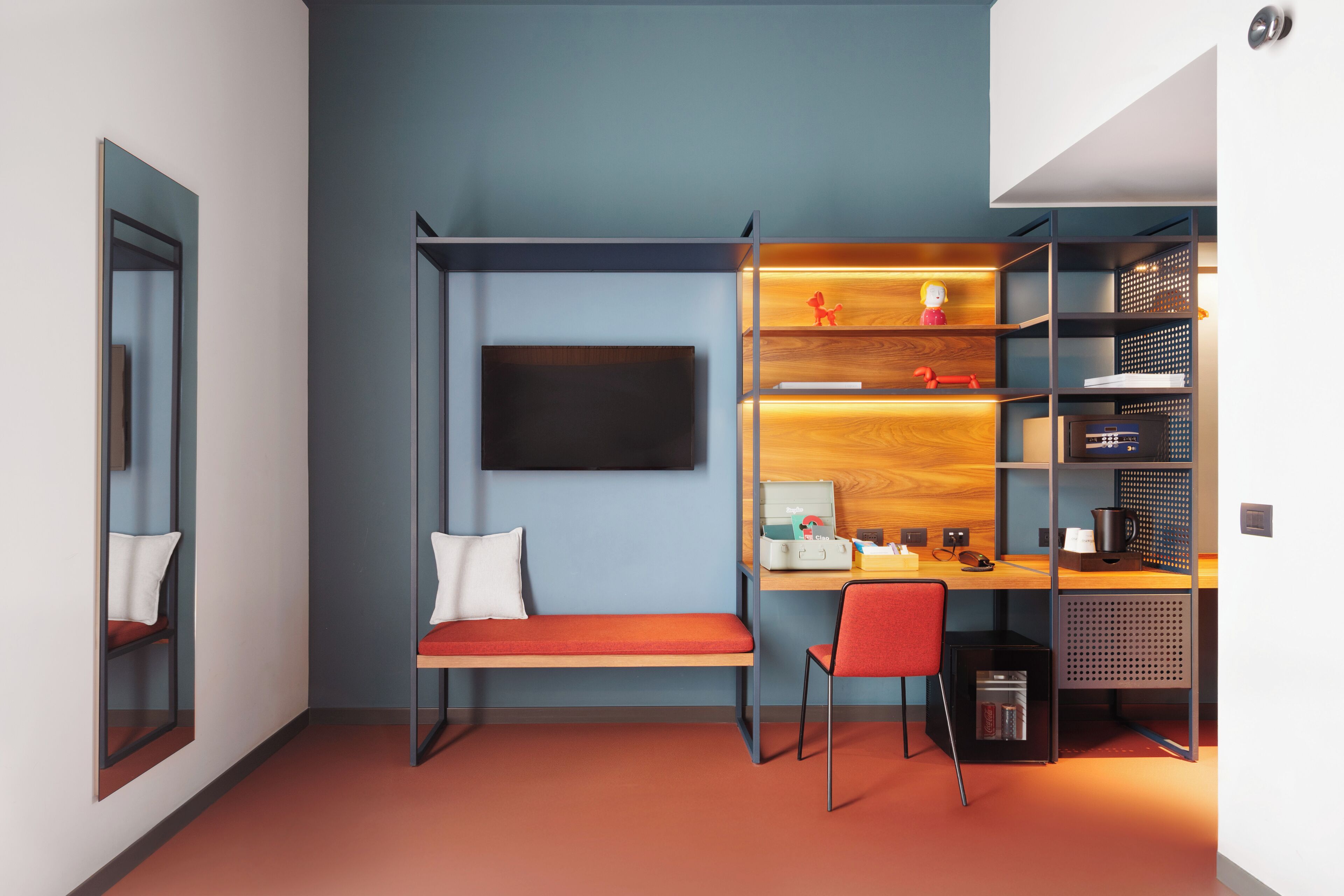 A modern room with a bench, a desk, a chair, a TV, and a bookshelf.