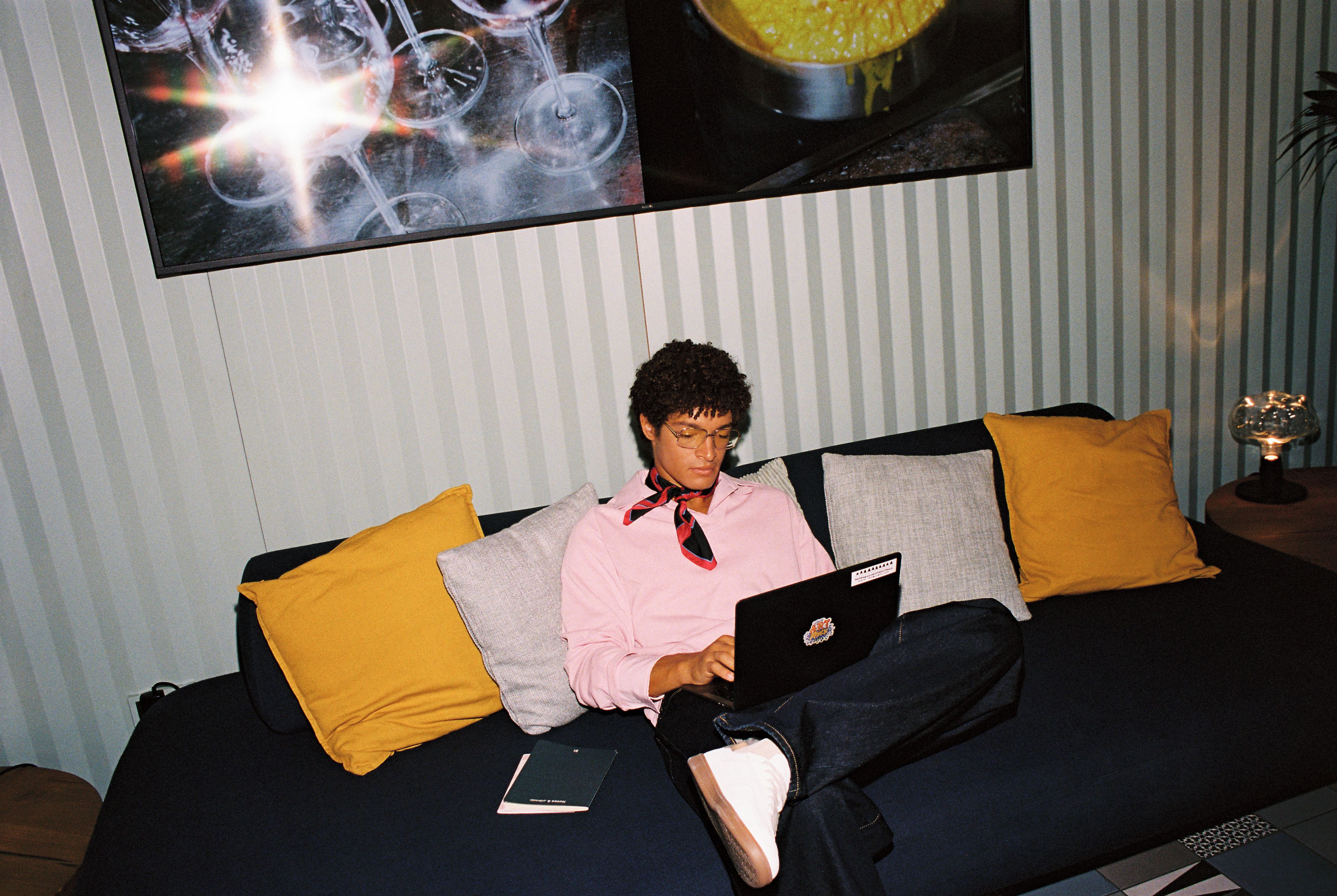 A person sitting on a couch with a laptop, a book, and a remote control.