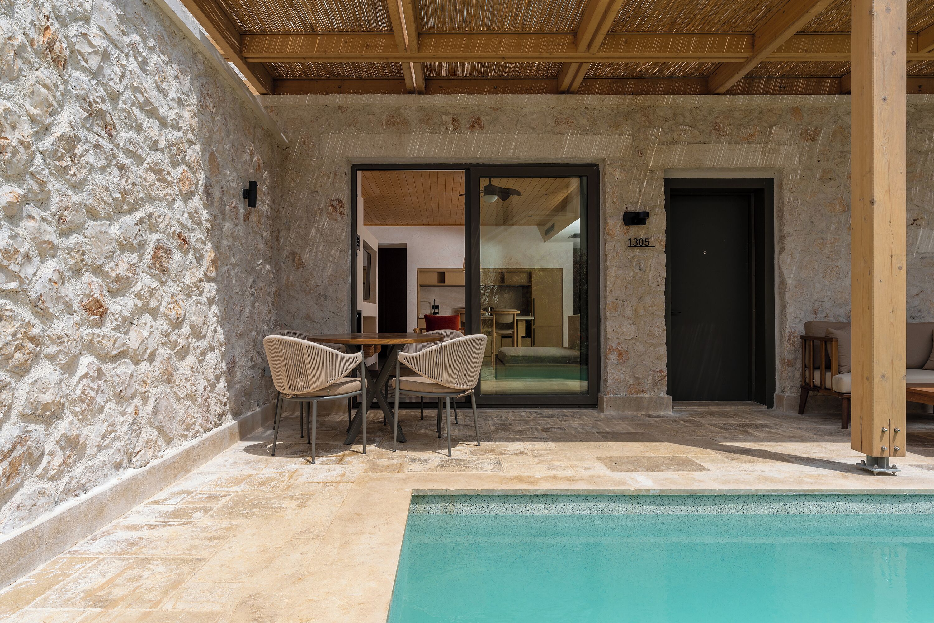 Ein Außenbereich mit Steinmauern, einem Pool, zwei Korbstühlen und einem Holztisch.