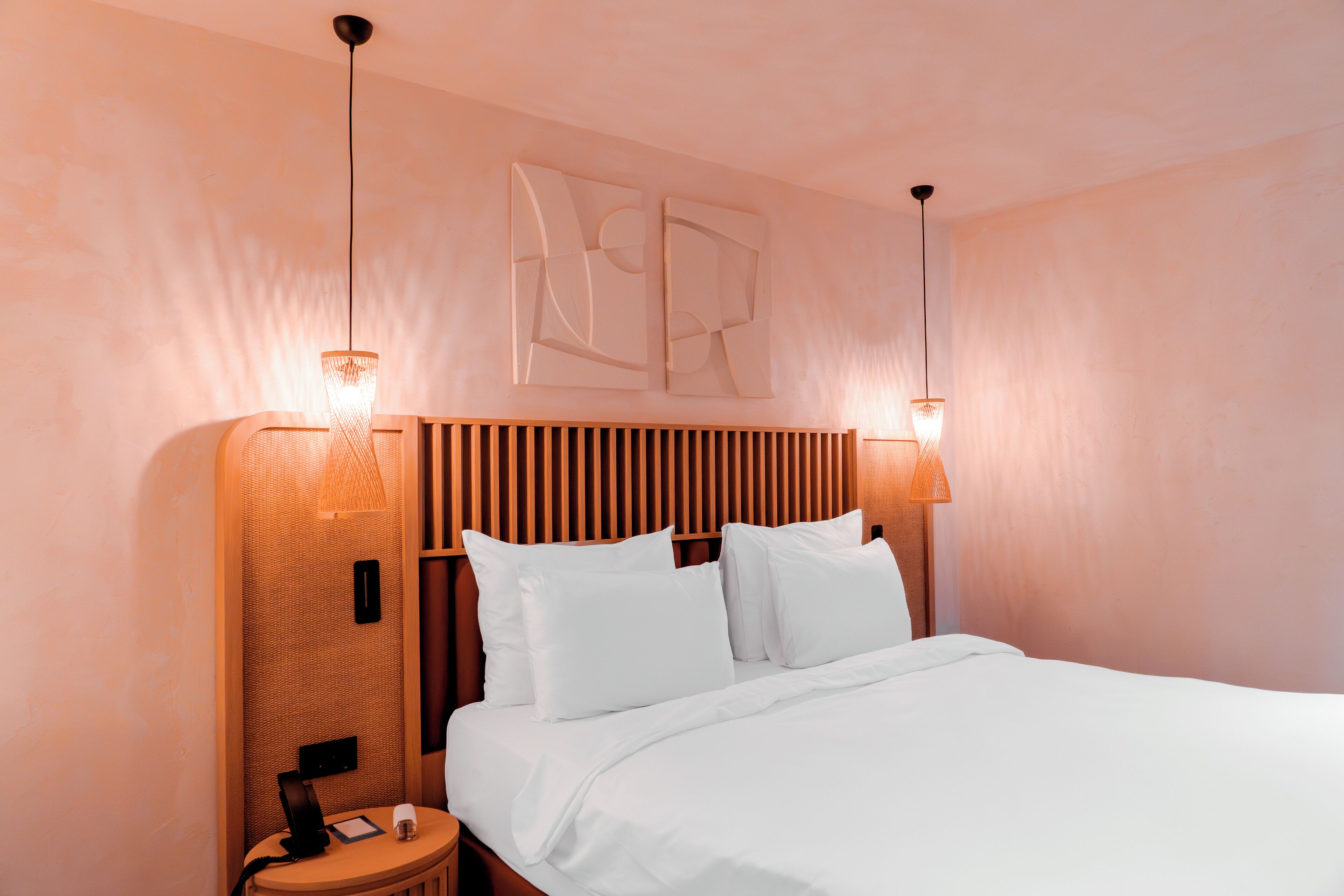 A neatly made bed with white linens, a wooden headboard, and two wall-mounted lamps.