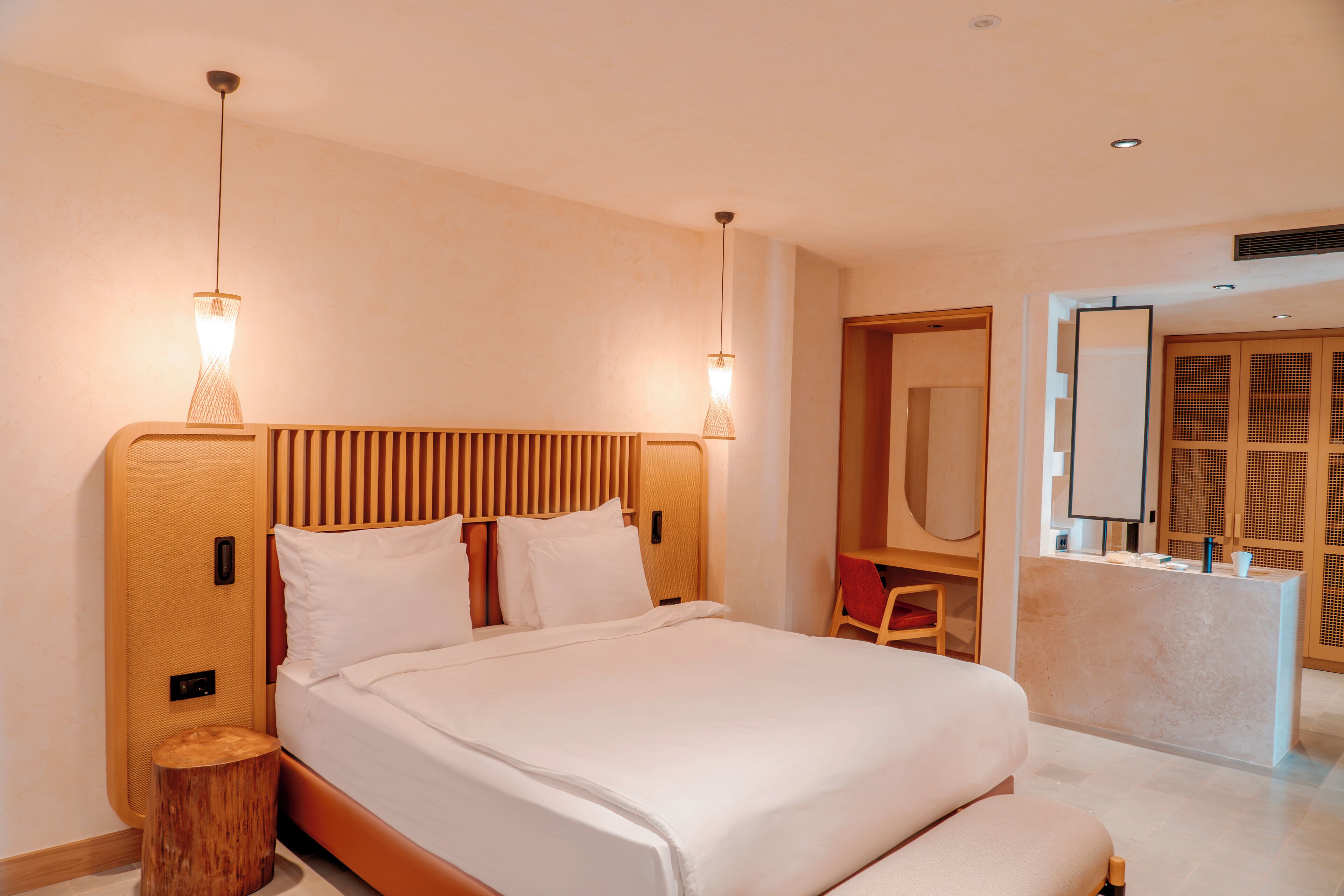 A modern hotel room with a large bed, wooden headboard, bedside tables, and a seating area with a chair and table.