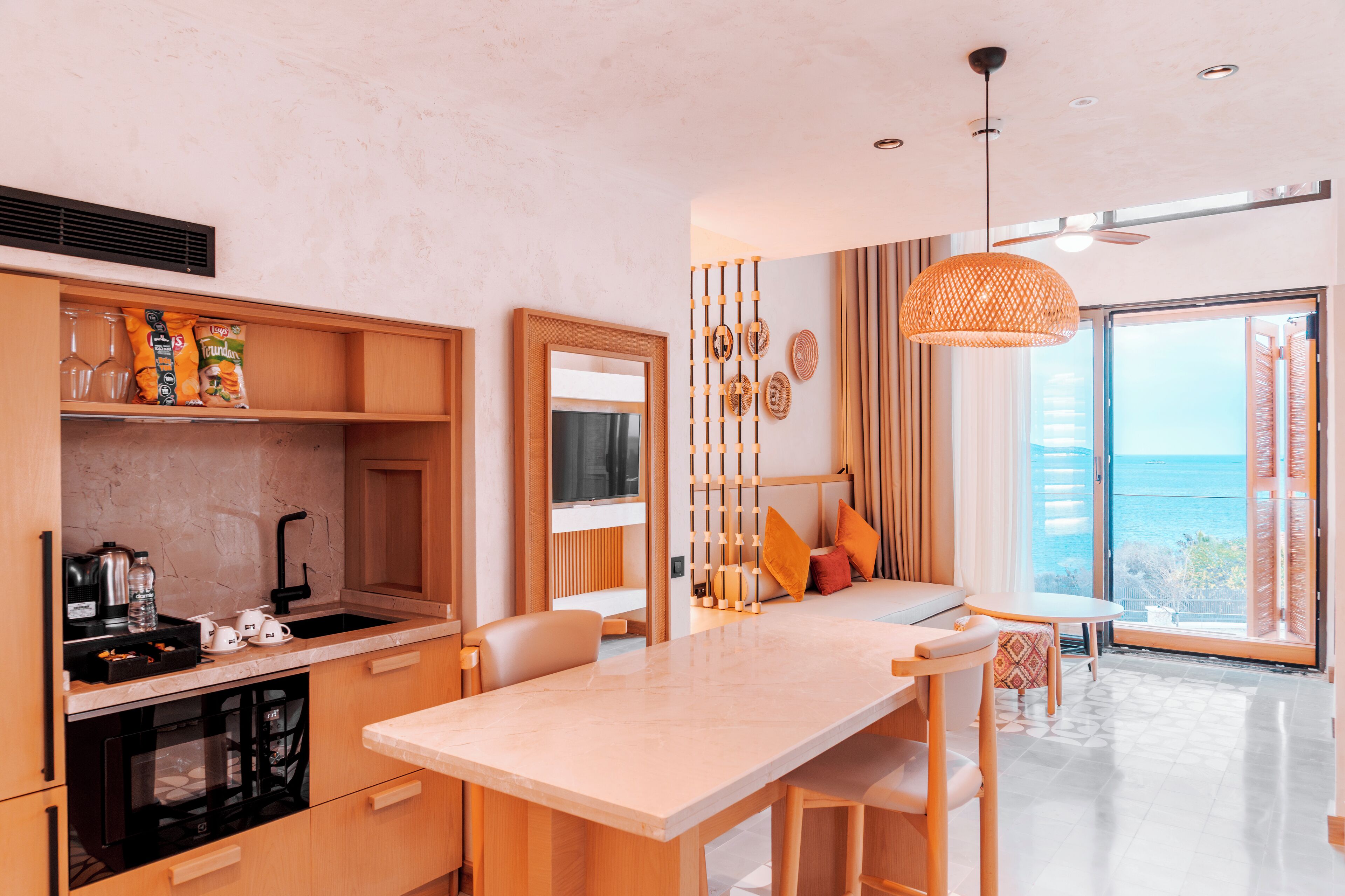A modern kitchen with a dining area, a large window with a view of the sea, and a ceiling fan.