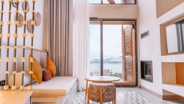 Habitación de hotel moderna con sofá, una mesita redonda, vista al mar y ventilador de techo.