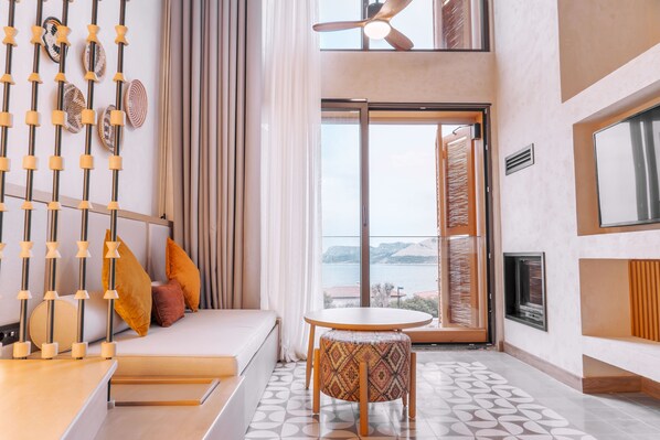 Une chambre d’hôtel moderne avec un canapé, une petite table ronde, une vue sur la mer et un ventilateur de plafond.