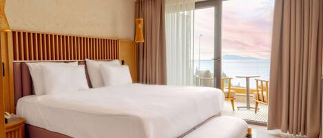 A hotel room with a large bed, a bench, a small table, and a view of the sea.